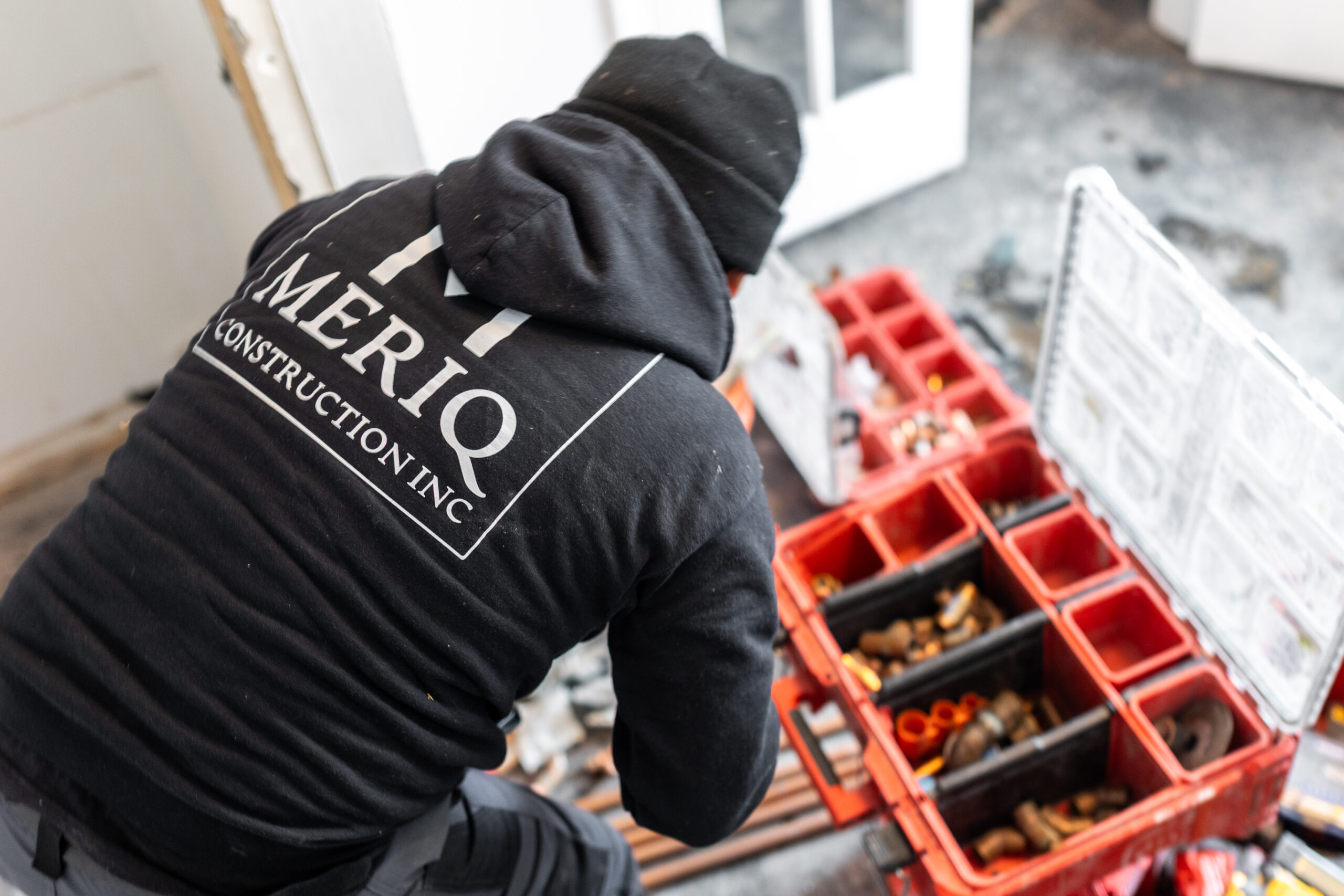 Meriq Construction Inc technician organizing plumbing fittings and tools during a home renovation project.