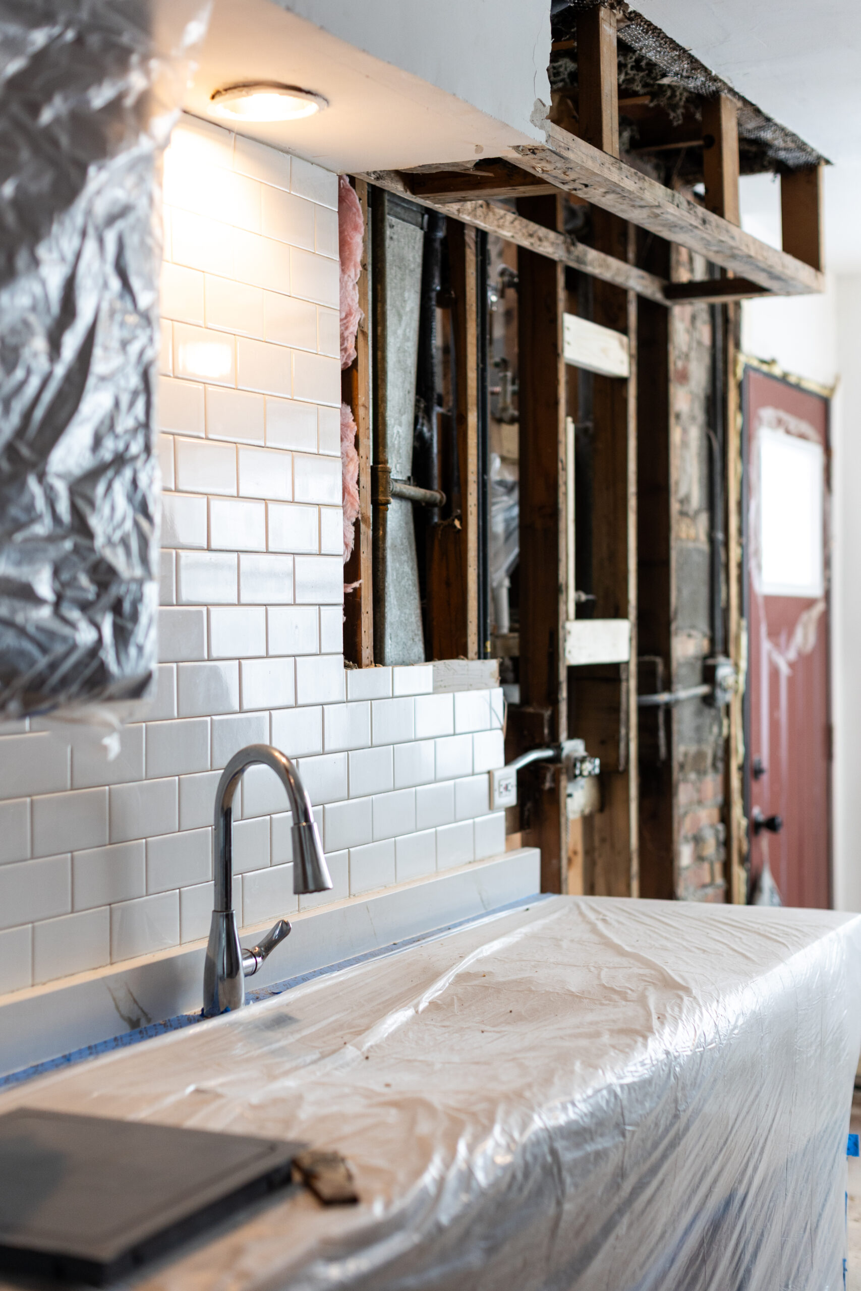 Kitchen renovation in progress showing wall framing, plumbing access, and tile backsplash installation by Meriq Construction Inc.