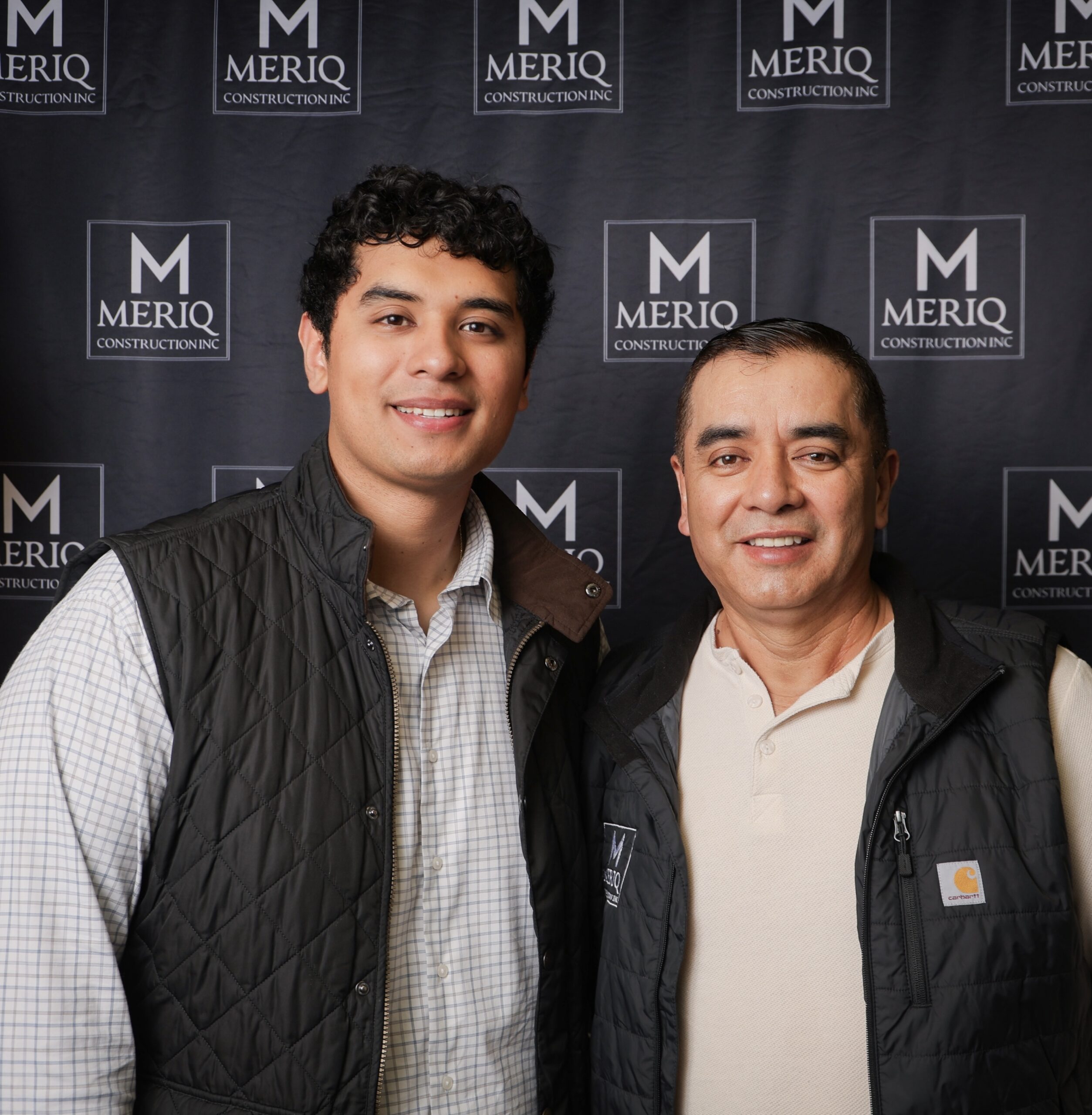 Founders of Meriq Construction Inc. standing together in front of the company’s branded backdrop.
